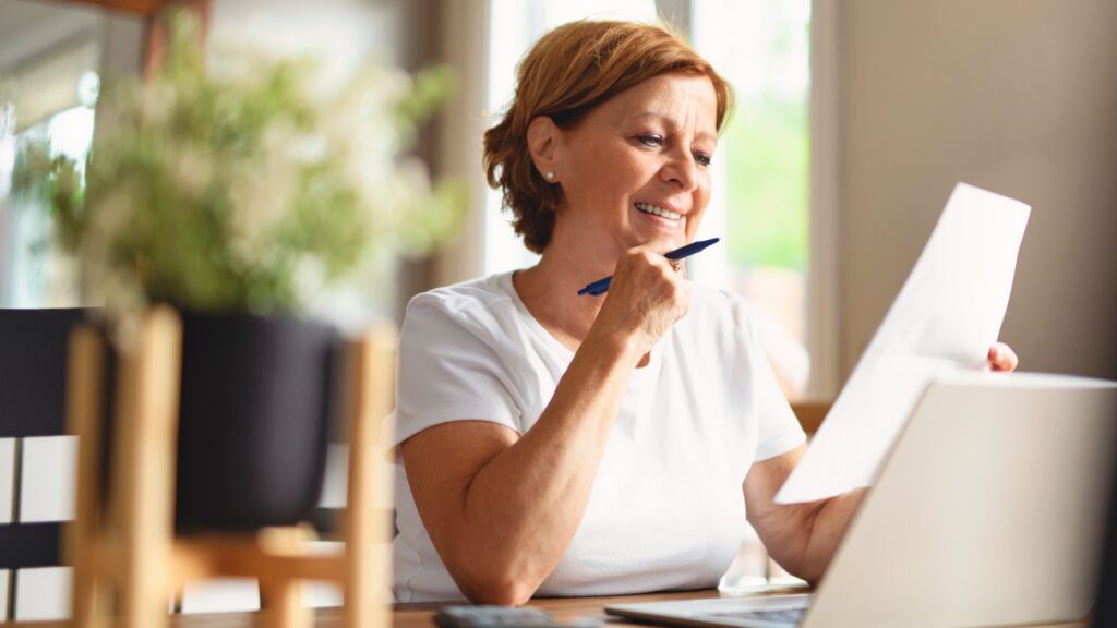 Woman in white shirt reviewing documents with laptop